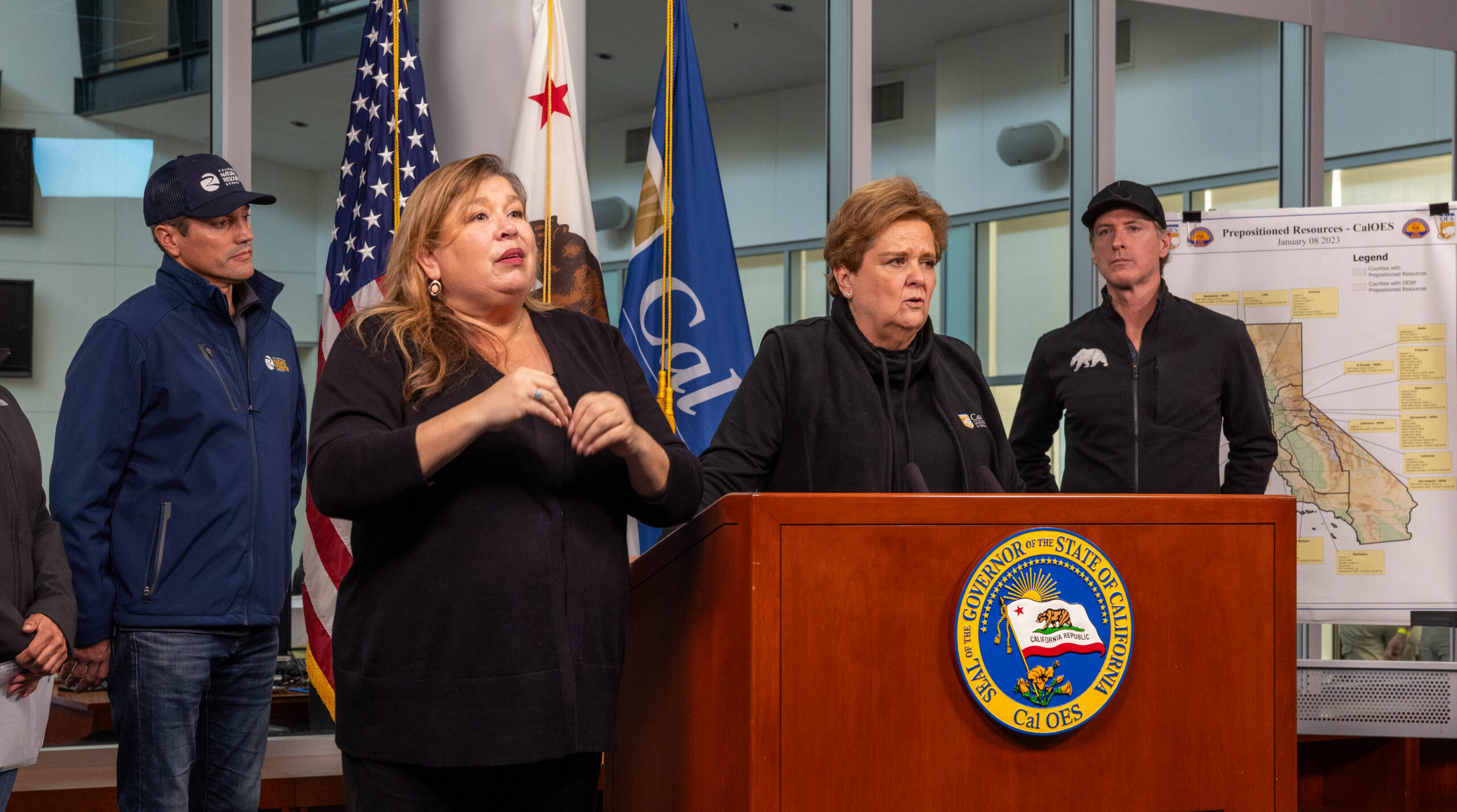 Nancy Ward standing at podium during a press conference, flanked by the ASL interpreter and Governor Gavin Newsom