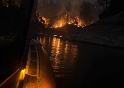 Fire burning on a hill from the view of a fire boat on a lake.