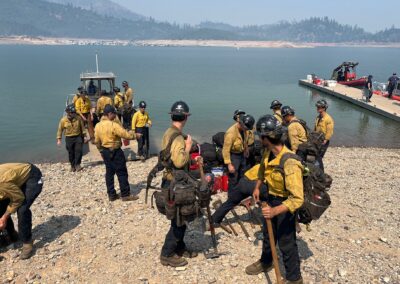 Firefighters preparing their equipment on the shore of a lake by a boat.