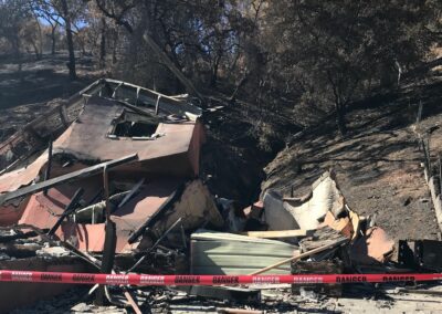 A building burned by wildfire with scorched land behind it.