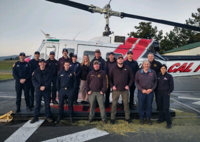 An multi-agency team stands in front of a CalFire helicopter.